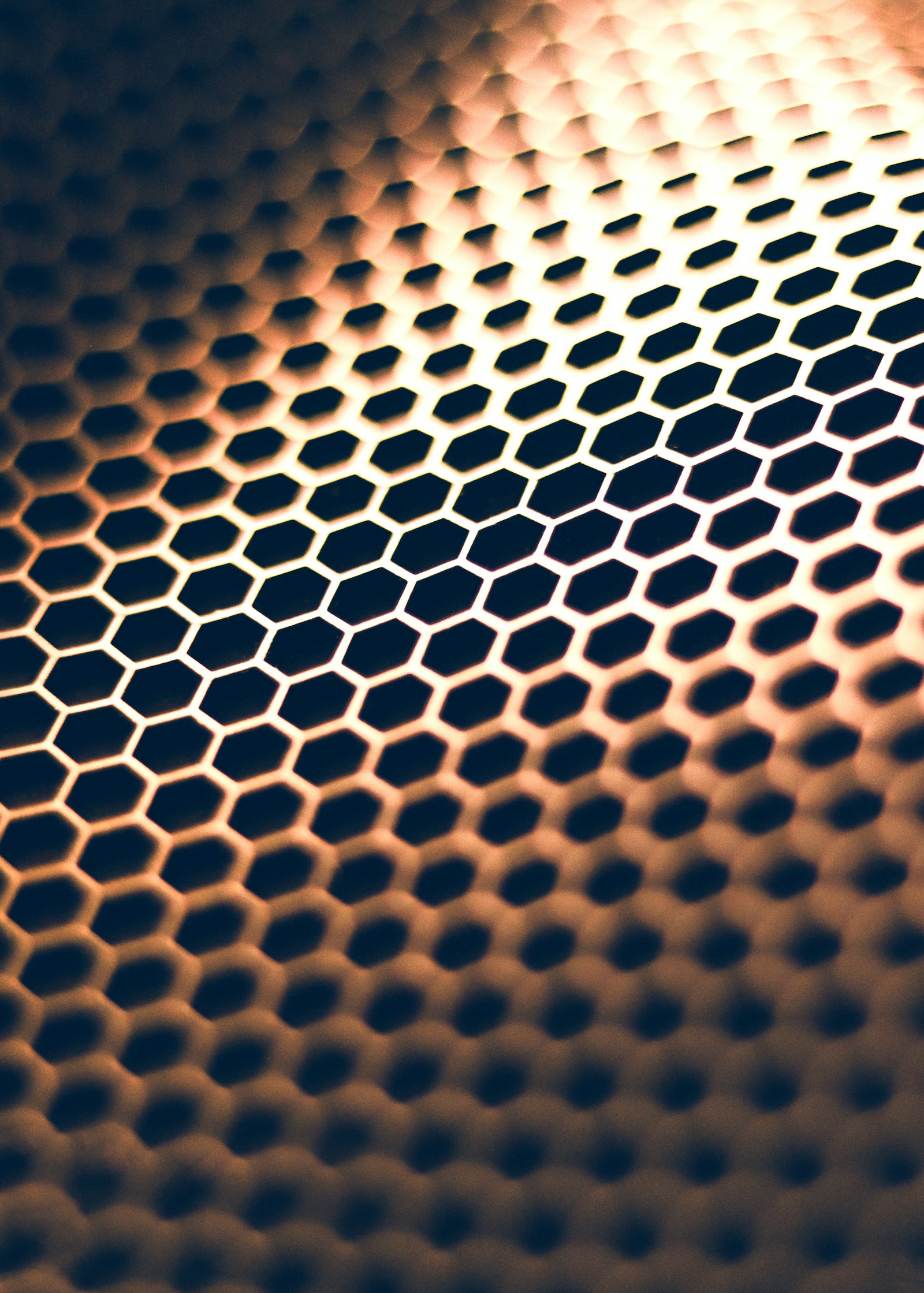 Hexagonal honeycomb lattice pattern in amber and shadow — the structural motif of graphene, a single atom-thick sheet of carbon arranged exactly this way