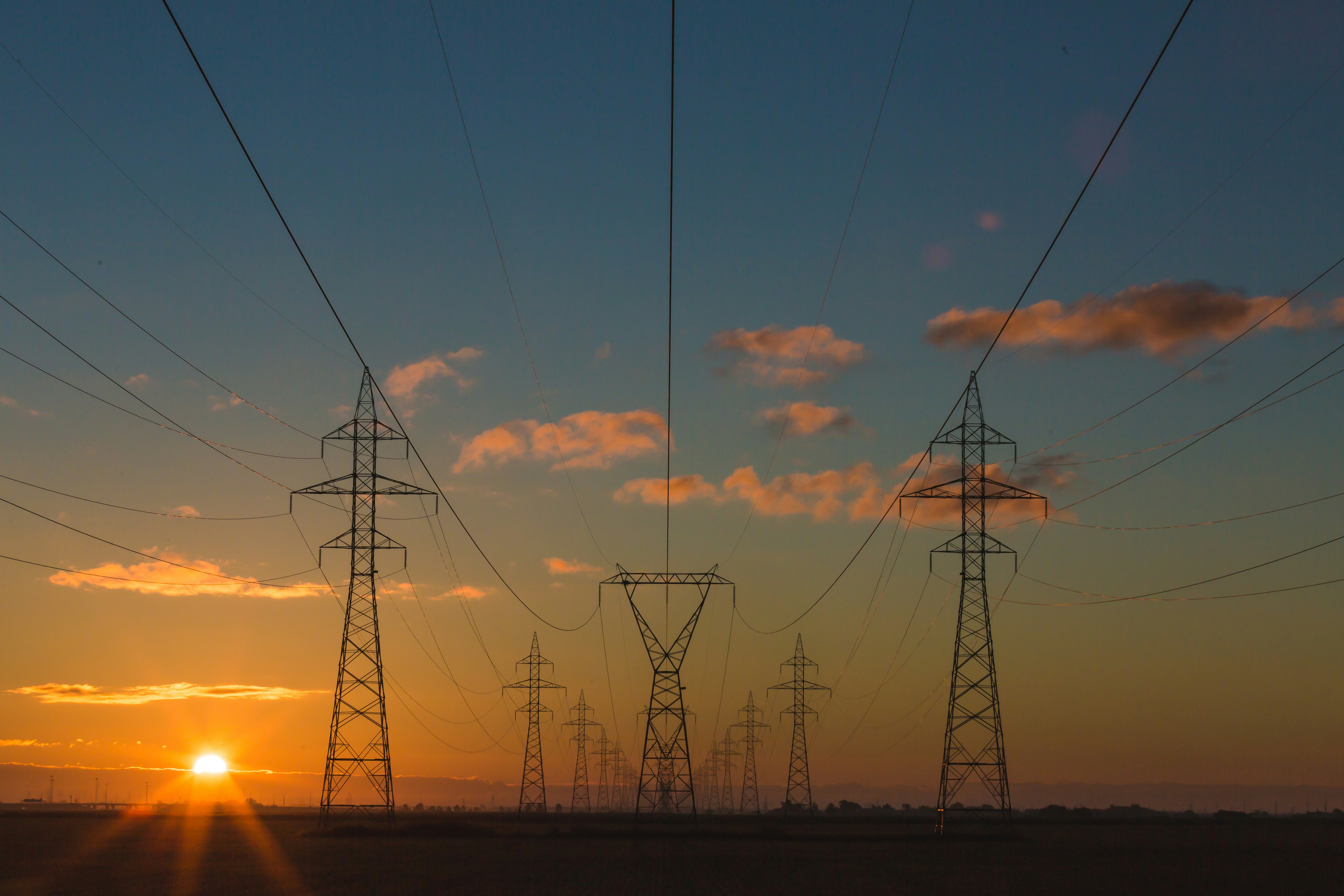 High-voltage transmission pylons against open sky — physical capital at scale