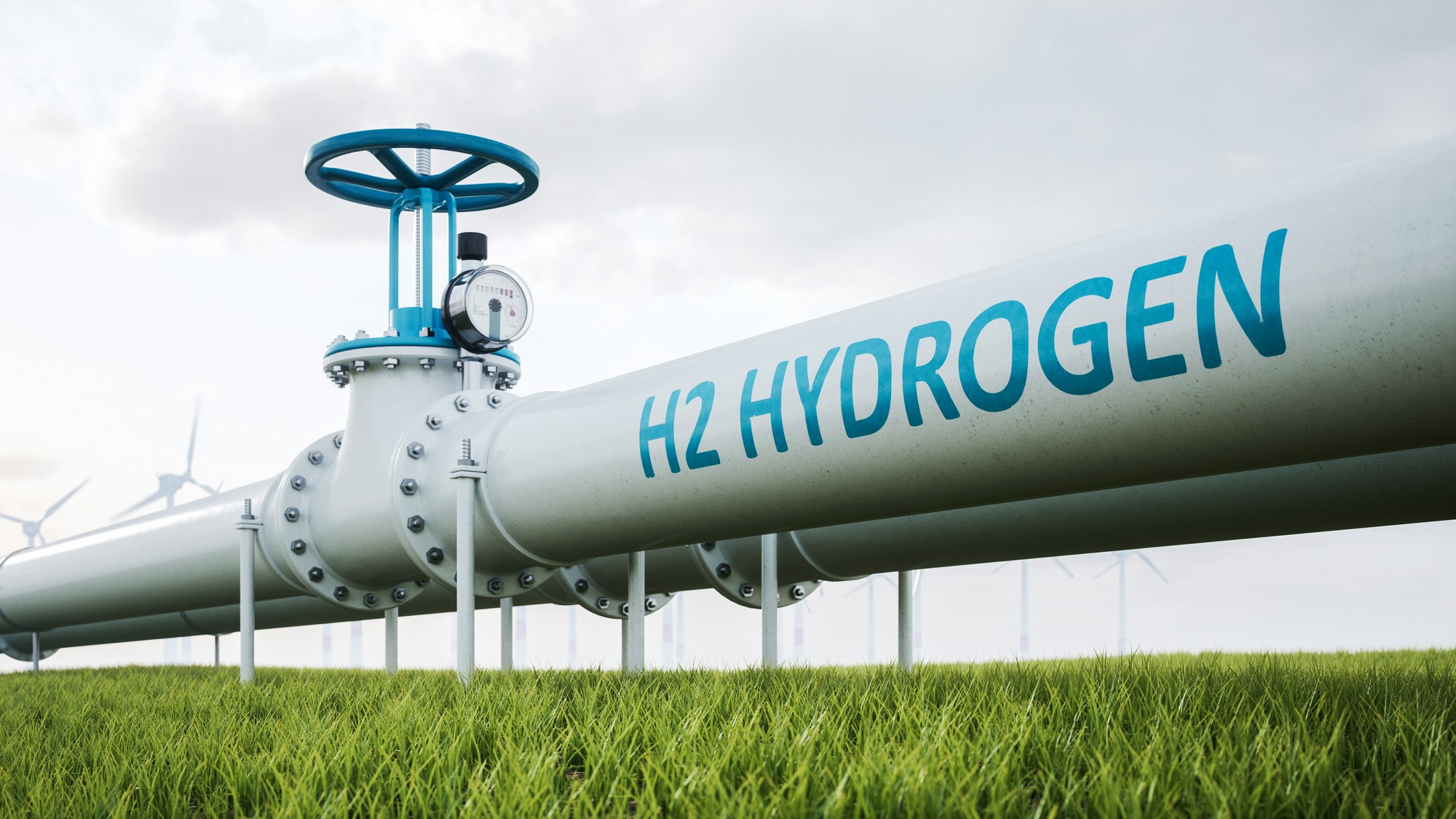 A white hydrogen pipeline marked H2 Hydrogen, with a blue valve wheel and pressure gauge, running across a green field with wind turbines in the distance