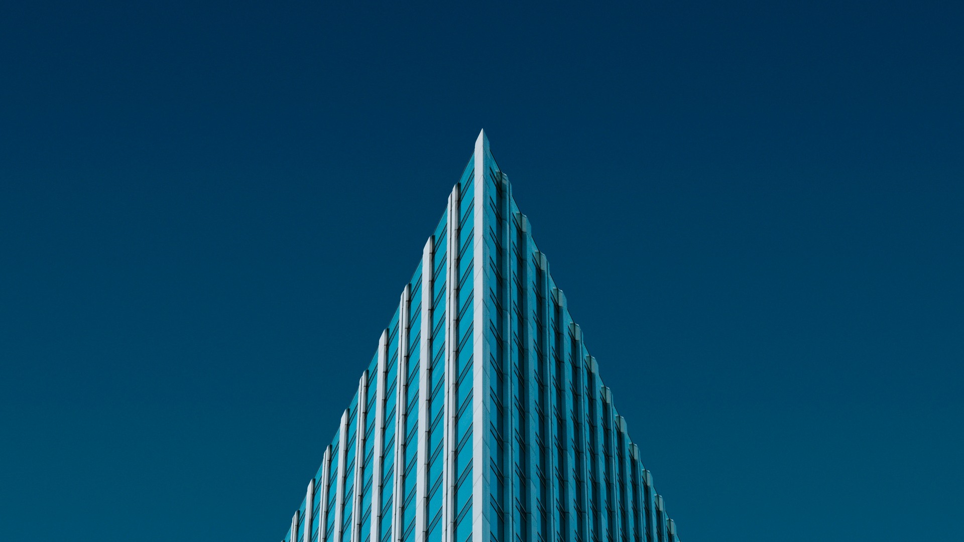 Low-angle view of a glass office tower, its corner rising to a sharp point against a deep blue sky