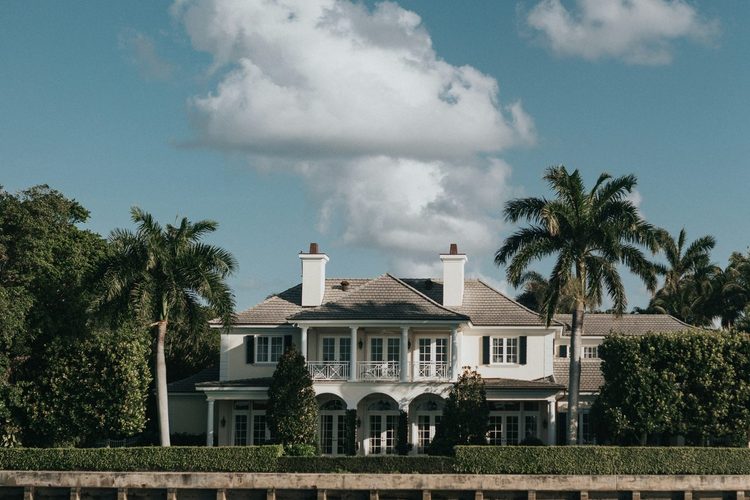 A waterfront estate seen from the water behind its sea wall and hedge line